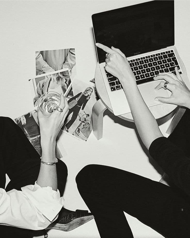Duas pessoas trabalhando com referências impressas e notebook